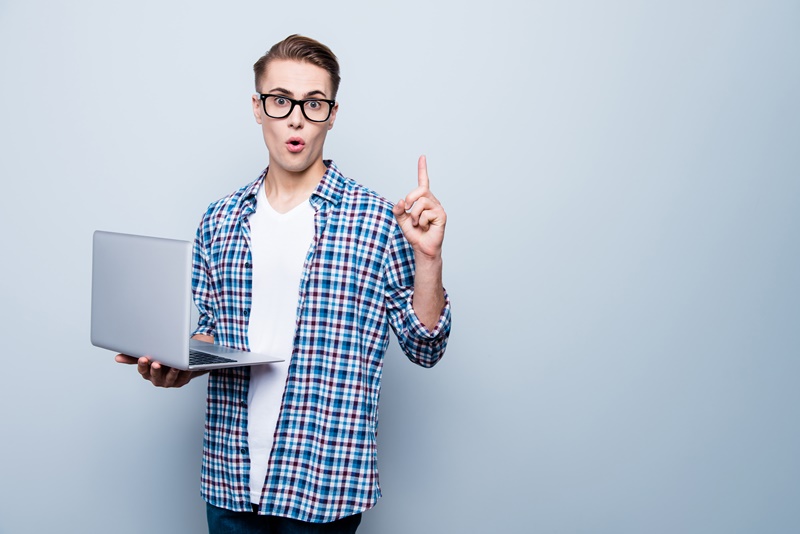 I know what to do! Close up portrait of smart teen look at camera with open mouth and big eyes, hold laptop and show forefinger up isolated on light blue background with copy space for text